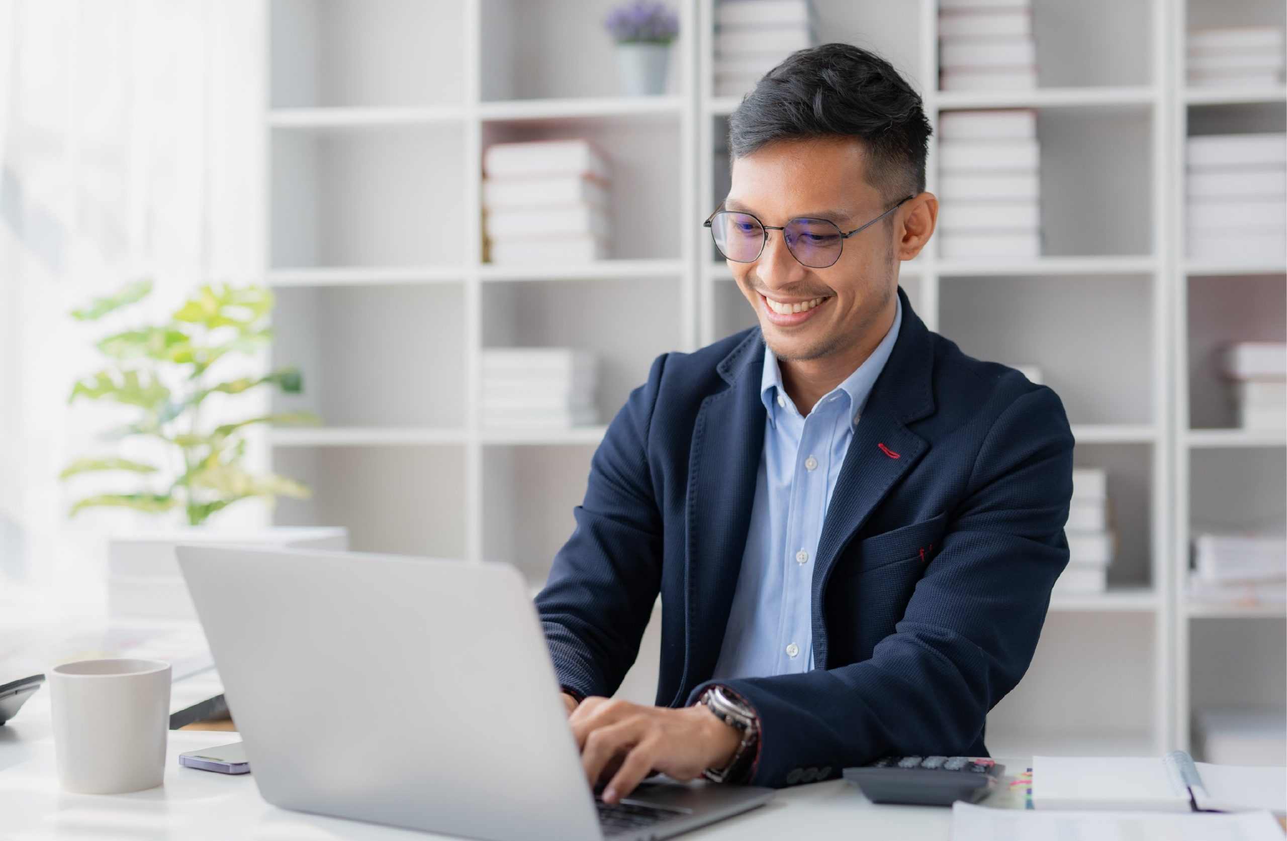 Man in glasses and business casual clothes smiling while typing on a laptop